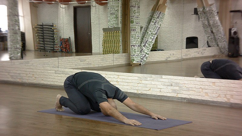 Man resting in child's pose with arms stretched forward on a mat (Wikimedia Commons photo)