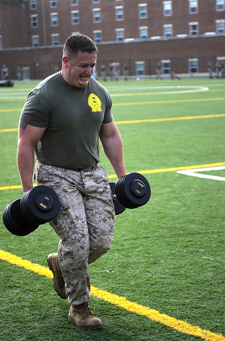 Marine walking while carrying a heavy dumbbell in each hand in a farmer's walk (Wikimedia Commons photo)